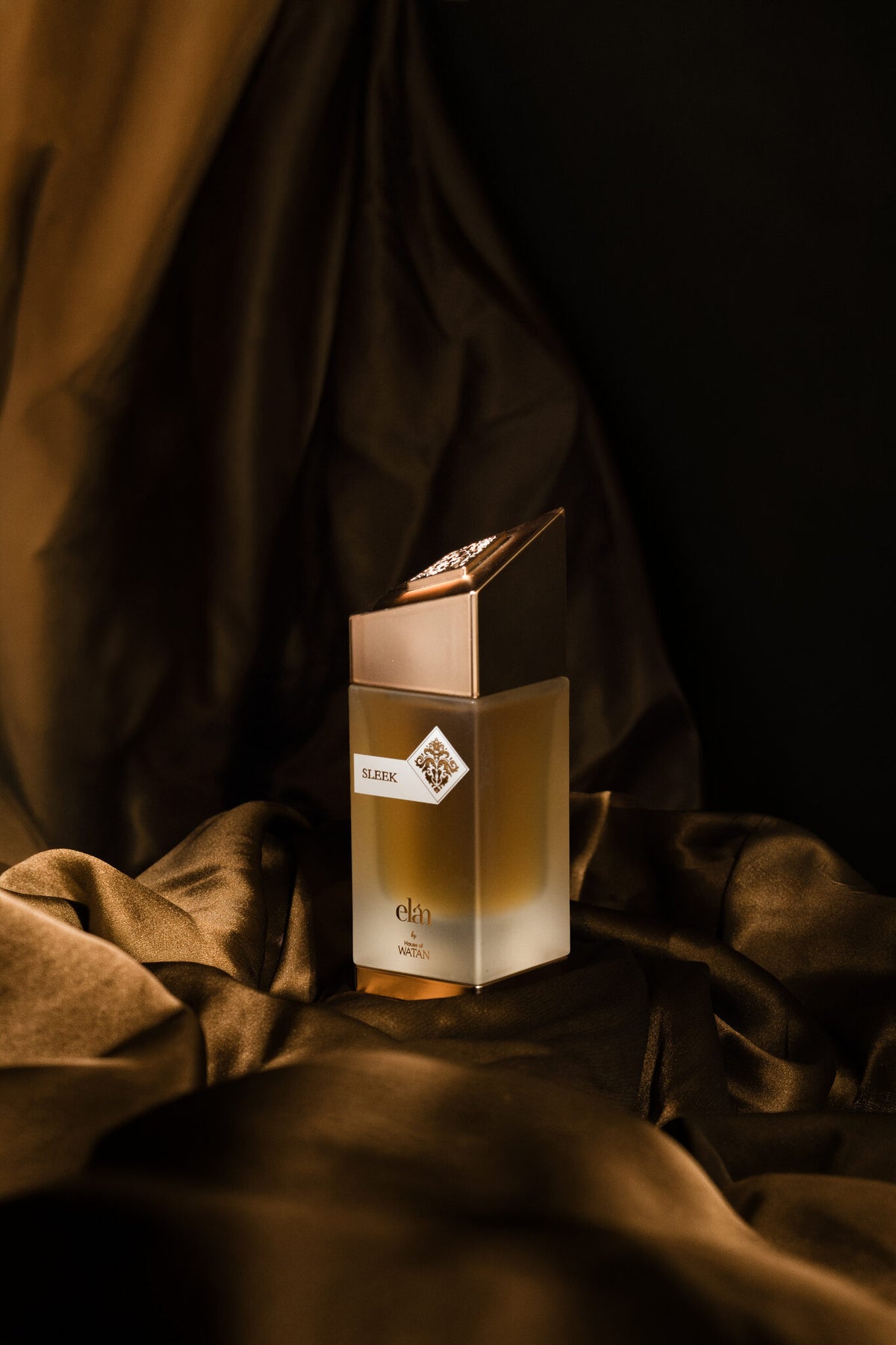 Sleek gold bottle on draped silk, warm gourmand fragrance