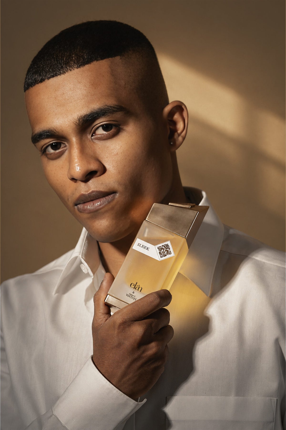 Model holding Sleek Eau de Parfum, unisex gold fragrance